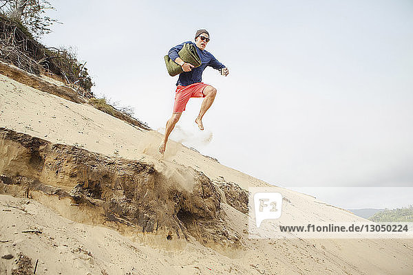 Man jumping from sand dune at beach