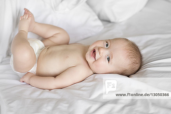 High angle portrait of cute shirtless baby boy lying on bed at home