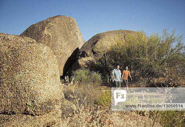 Happy couple walking on dirt road by rock foramtions against clear blue sky