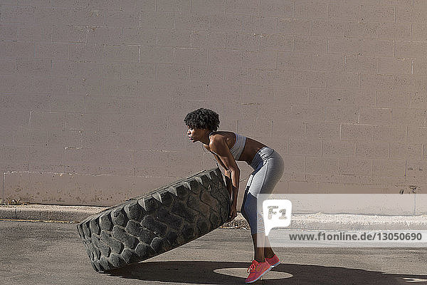 Woman lifting tire truck while exercising against wall