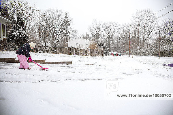 Seitenansicht eines Mädchens  das im Hinterhof Schnee mit einer Schaufel räumt