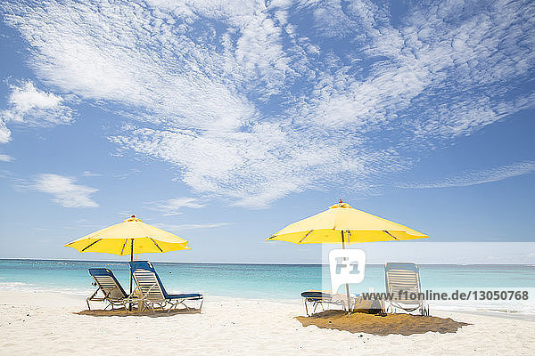 Szenerieansicht von Sonnenschirmen und Liegestühlen am Strand bei bewölktem Himmel am sonnigen Tag