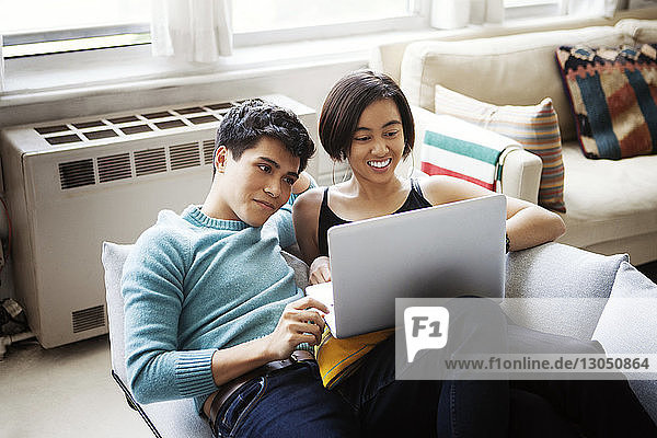 Happy young couple using laptop while reclining on sofa at home