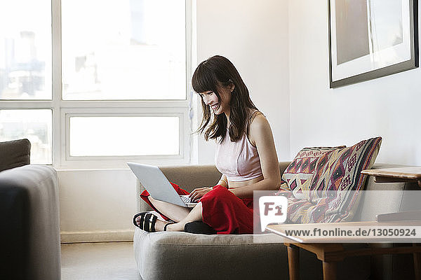 Lächelnde Frau benutzt Laptop  während sie im Büro auf dem Sofa sitzt