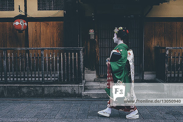 Seitenansicht einer Frau in traditioneller Kleidung  die auf einem Fußweg am Haus entlang geht