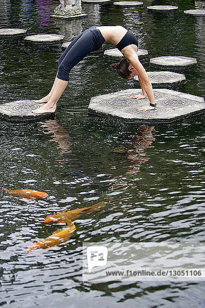 Seitenansicht einer Frau  die ihre Brückenposition auf Plattformen inmitten eines Teiches im Park übt