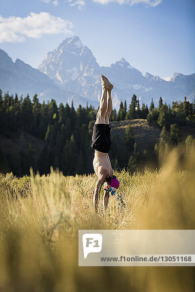 Shirtless man doing handstand while practicing yoga against mountains on field at Bridger-Teton National Forest