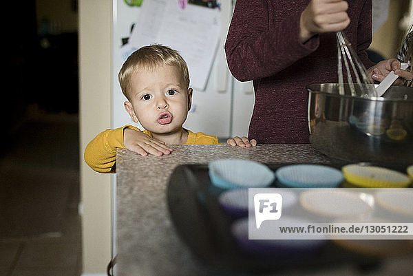 Portrait of cute boy standing by brother preparing food in kitchen