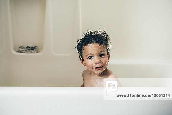 Porträt eines hemdlosen  nassen Jungen  der zu Hause in der Badewanne sitzt