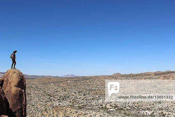 Mid distance view of male hiker standing on cliff against blue sky