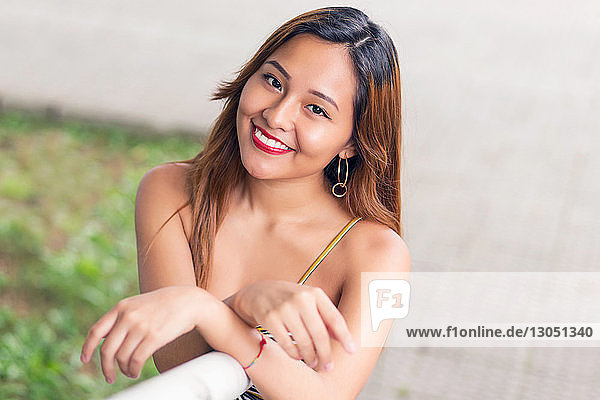 Hochwinkelporträt einer lächelnden jungen Frau  die am Geländer eines Parks steht