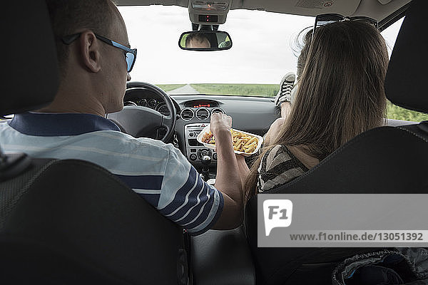 Rückansicht eines Paares  das Pommes Frites im Auto isst