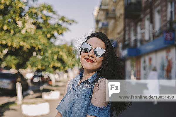 Lächelnde junge Frau mit Sonnenbrille  die in der Stadt steht