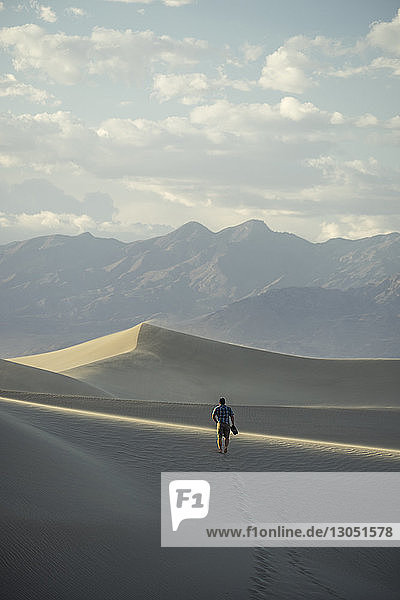 Rear view of hiker walking on desert against cloudy sky