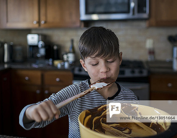 Junge isst Schokolade auf Spachtel  während er in der Küche steht