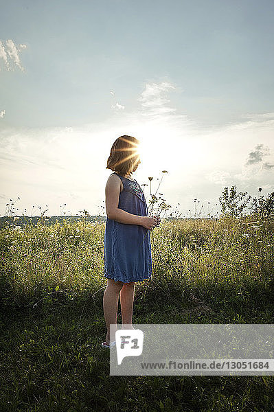 Girl holding flower while standing on grassy field against sky