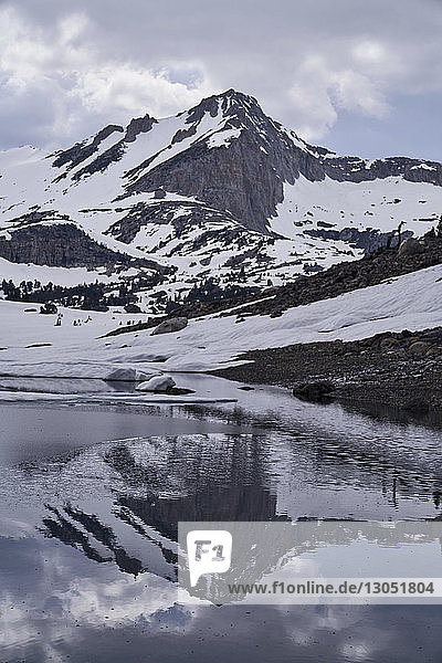 Landschaftliche Ansicht schneebedeckter Berge  die sich auf einem ruhigen See vor bewölktem Himmel spiegeln