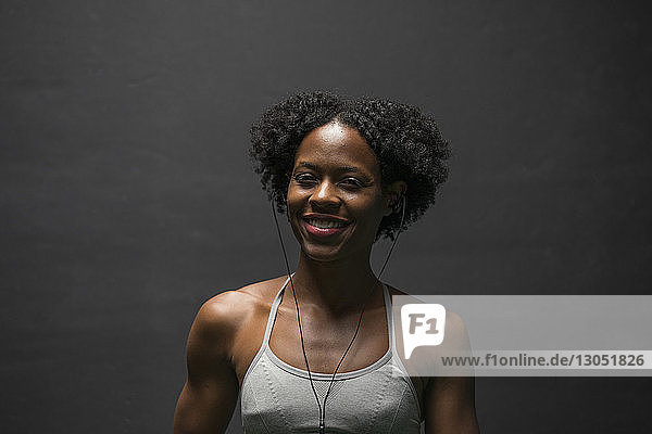 Portrait of cheerful woman listening music while exercising against wall in gym