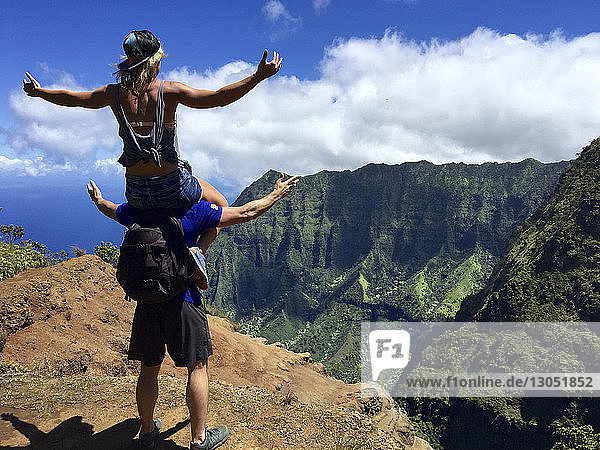 Rear view of man carrying woman on shoulder while standing on mountain against sky