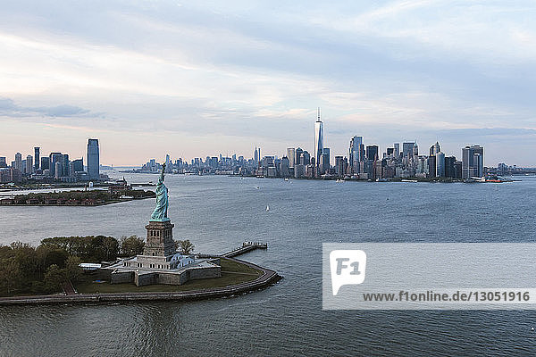 Statue of Liberty by island in city against cloudy sky