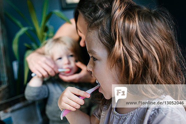 Mother helping children brush teeth
