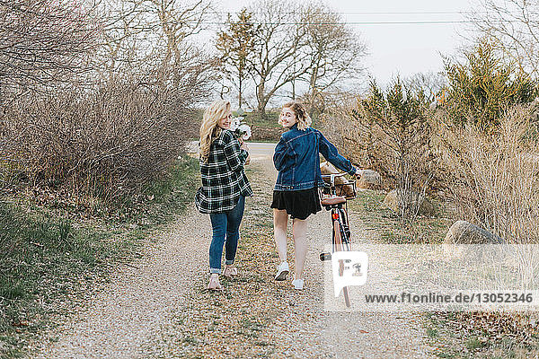 Zwei junge Frauen schieben Fahrrad auf ländlichem Feldweg, Porträt von hinten, Menemsha, Martha's Vineyard, Massachusetts, USA