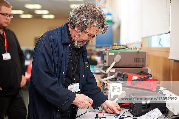 Dozent bereitet elektrisches Instrument vor  Student im Hintergrund