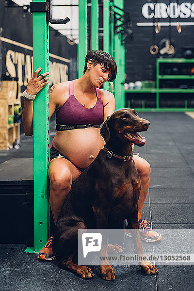 Schwangere Frau und Haushund sitzen in Turnhalle