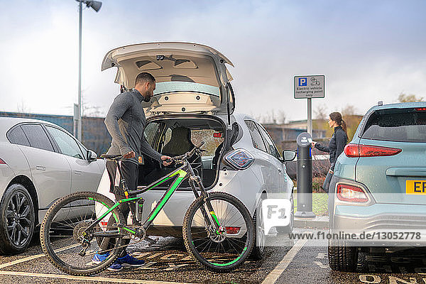 Man and woman with mountain bike at electric car charging point Manchester UK