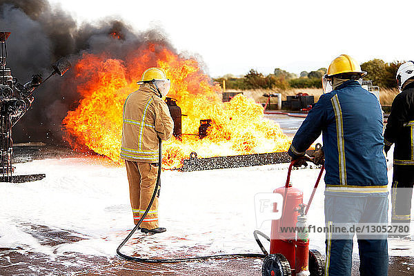 Firemen training  team of firemen spraying firefighting foam on fire at training facility  rear view