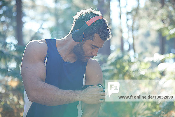 Männlicher Läufer mit Smartphone-Binde im sonnenbeschienenen Wald