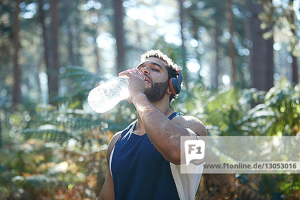 Männlicher Läufer trinkt Flaschenwasser im sonnenbeschienenen Wald