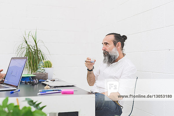 Hipster businessman drinking water at office desk