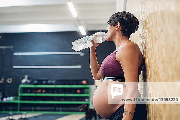 Schwangere Frau trinkt aus Wasserflasche im Fitnessstudio