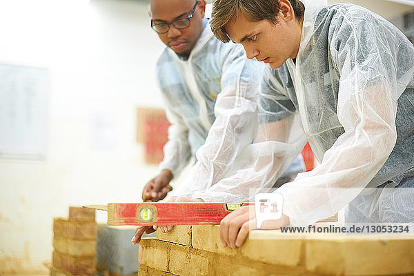 Male higher education students building brick wall in college workshop