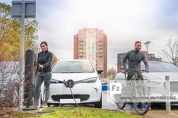 Mann und Frau mit Mountainbike an einer Ladestation für Elektroautos, Manchester, UK
