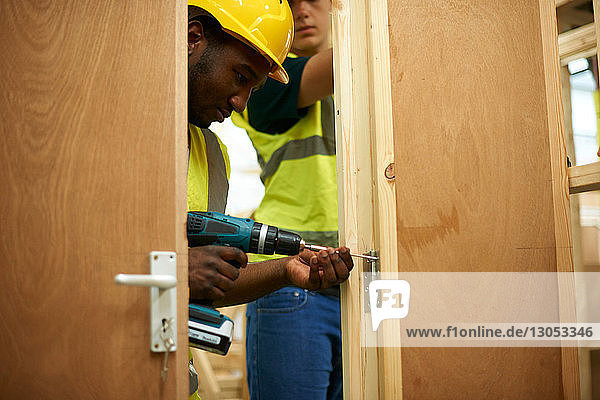 Male higher education students drilling wooden doorway in college workshop