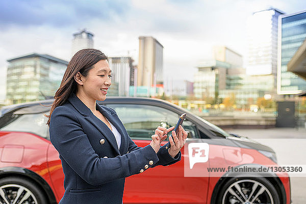 Woman checking electric car charge on mobile phone app Manchester UK