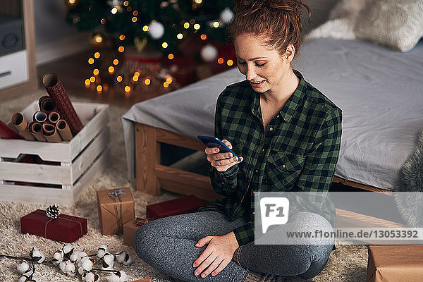 Frau textet beim Einpacken von Weihnachtsgeschenken