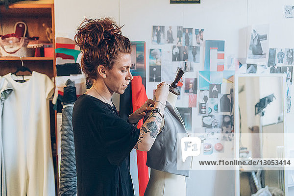 Modedesigner heftet Kleidungsstück an Schneiderpuppe