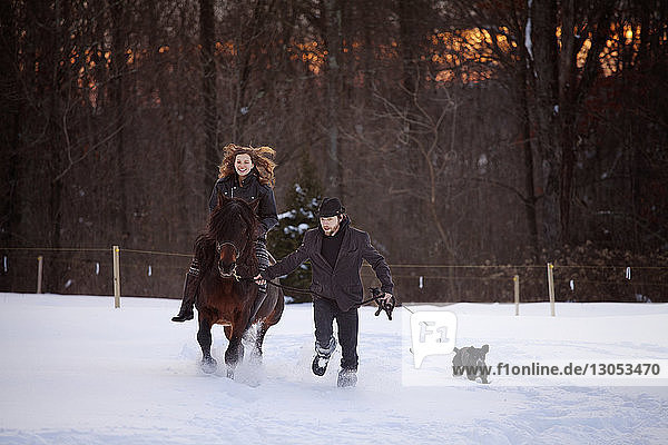 Mann hält Seil  während Frau auf schneebedecktem Feld reitet