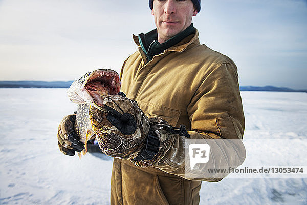 Ausgewachsener Mann hält Fisch am gefrorenen See