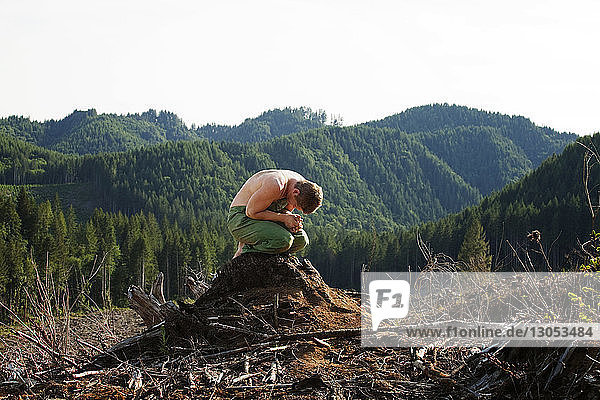 Mann kniend auf Baumstumpf gegen Wald