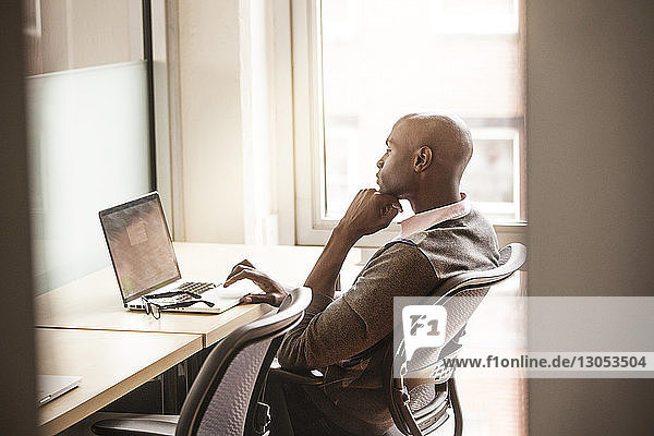 Seitenansicht eines Geschäftsmannes  der einen Laptop benutzt  während er im Büro sitzt