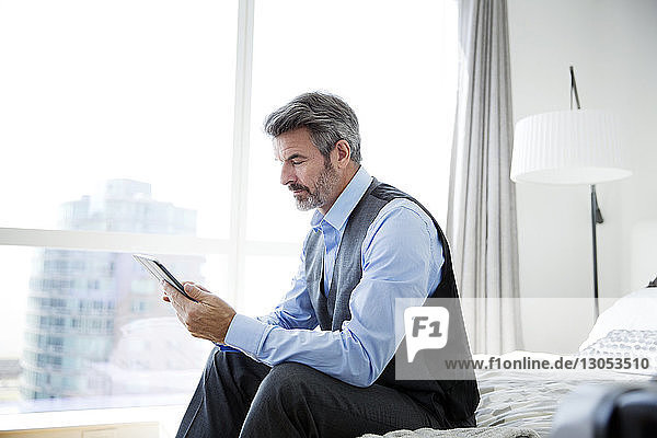 Geschäftsmann benutzt Tablet-Computer  während er auf dem Bett am Fenster sitzt