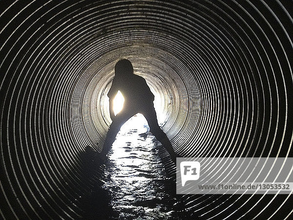 Rückansicht eines im Abwassertunnel stehenden Scherenschnitt-Jungen