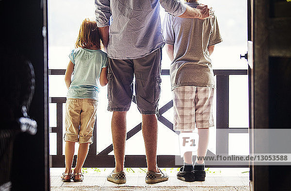 Rückansicht von Vater und Kindern  die auf dem Balkon stehen  durch die Tür gesehen