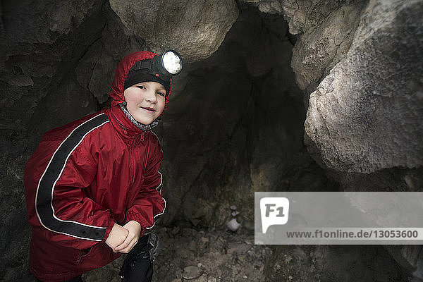 Portrait of boy wearing headlamp while standing by rock formations in cave