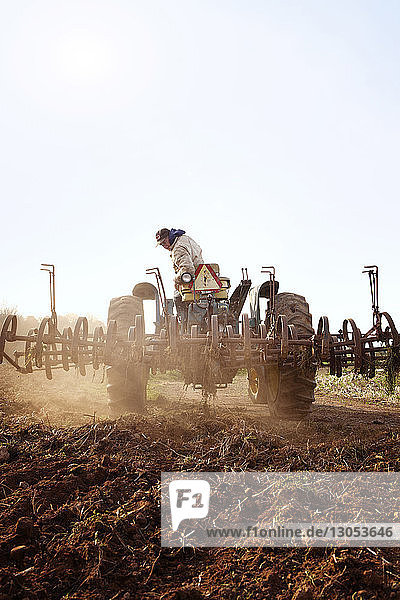 Farmer driving tractor on field against clear sky