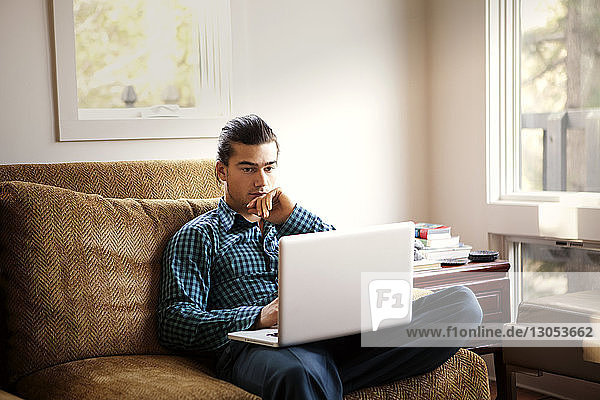 Man using laptop computer while sitting on sofa at home